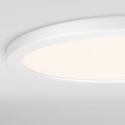 A close-up of the Skylight Pro 15" 5K LED Flat Panel Light shows its ultra-slim, round, white design with a soft glow on a light gray ceiling and adjustable brightness for personalized ambiance.