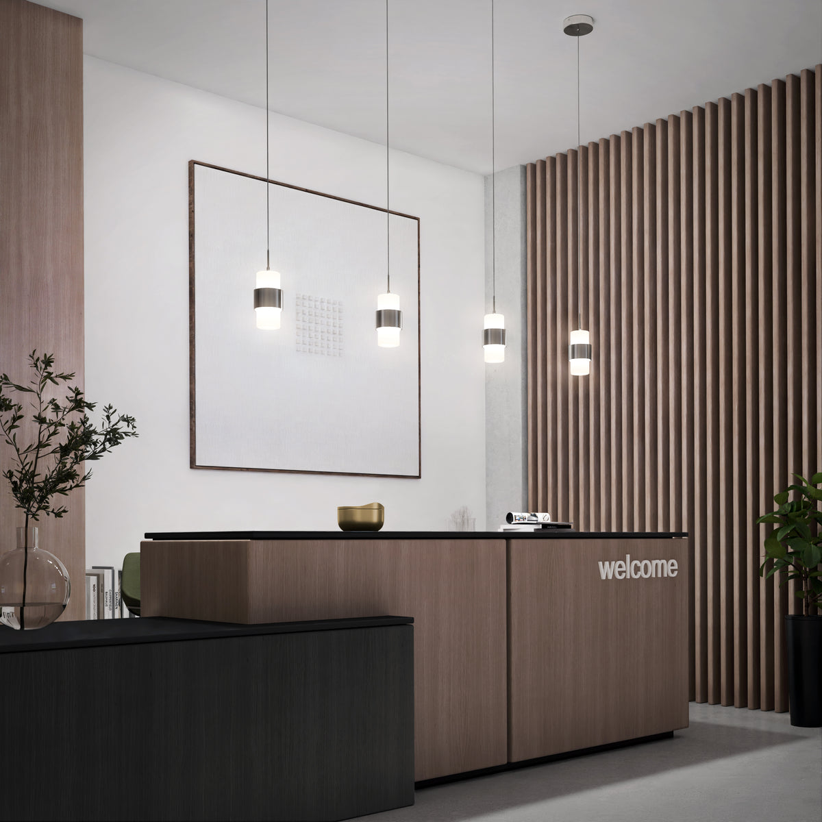 Modern reception area with a sleek black and wood front desk labeled "welcome." Miko 3CCT LED Mini Pendants hang above, while wooden slats, plants, and large framed artwork enhance the minimalist décor.